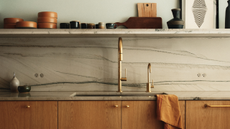 A white and oak kitchen with lighting hanging on top of an island. On the island is an arrangement of green foliage 