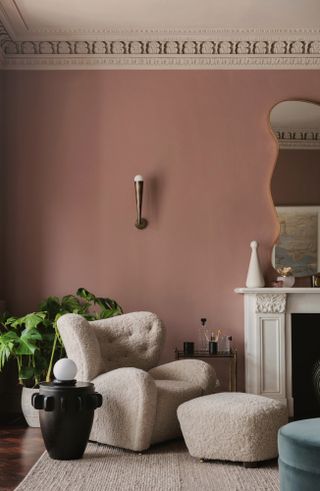 Pink living room with beige boucle armchair and footstool and black side table