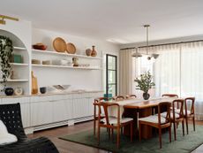 A dining room with a green rug, a light above the table and storage on the walls