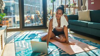 Home workout ideas: Woman sitting on a yoga mat in front of her laptop
