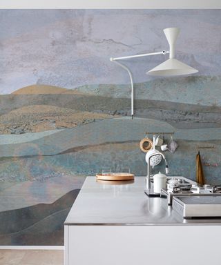 modern wallpaper mural with sweeping hills in shades of green, brown and blue, white metal wall light and white and chrome kitchen island