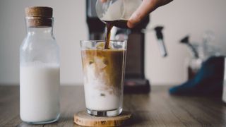 an iced coffee in front of a coffee maker with milk at the side
