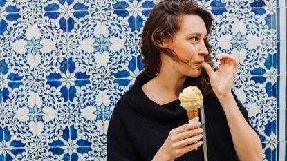 Millennial woman licking finger while eating ice cream at a tiled wall, to illustrate destinations for solo travel