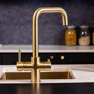 A brass-coated boiling water tap in a dark blue kitchen