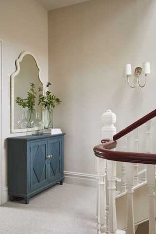 Landing with neutral decor, blue cabinet with mirror above, and wall light