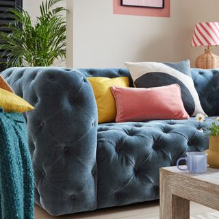 A blue quilted sofa with three multi-coloured cushions asymmetrically arranged on top