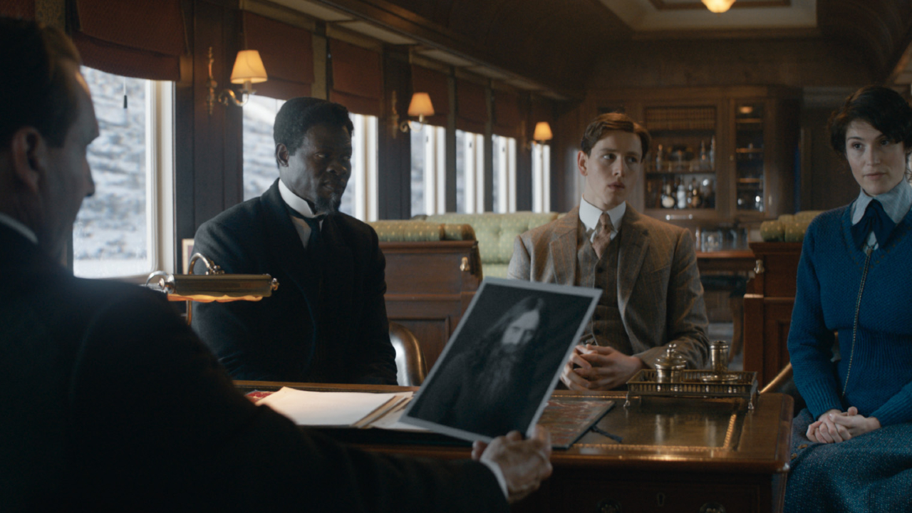 Ralph Fiennes, Djimon Honsou, Harris Dickinson, and Gemma Arterton meet in a train car in The King's Man.