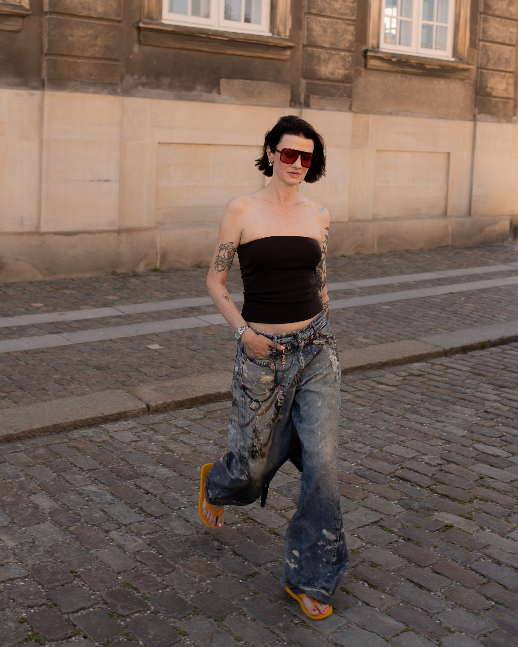A woman at Copenhagen Fashion Week in a black tube top, distressed jeans, and orange flip flops