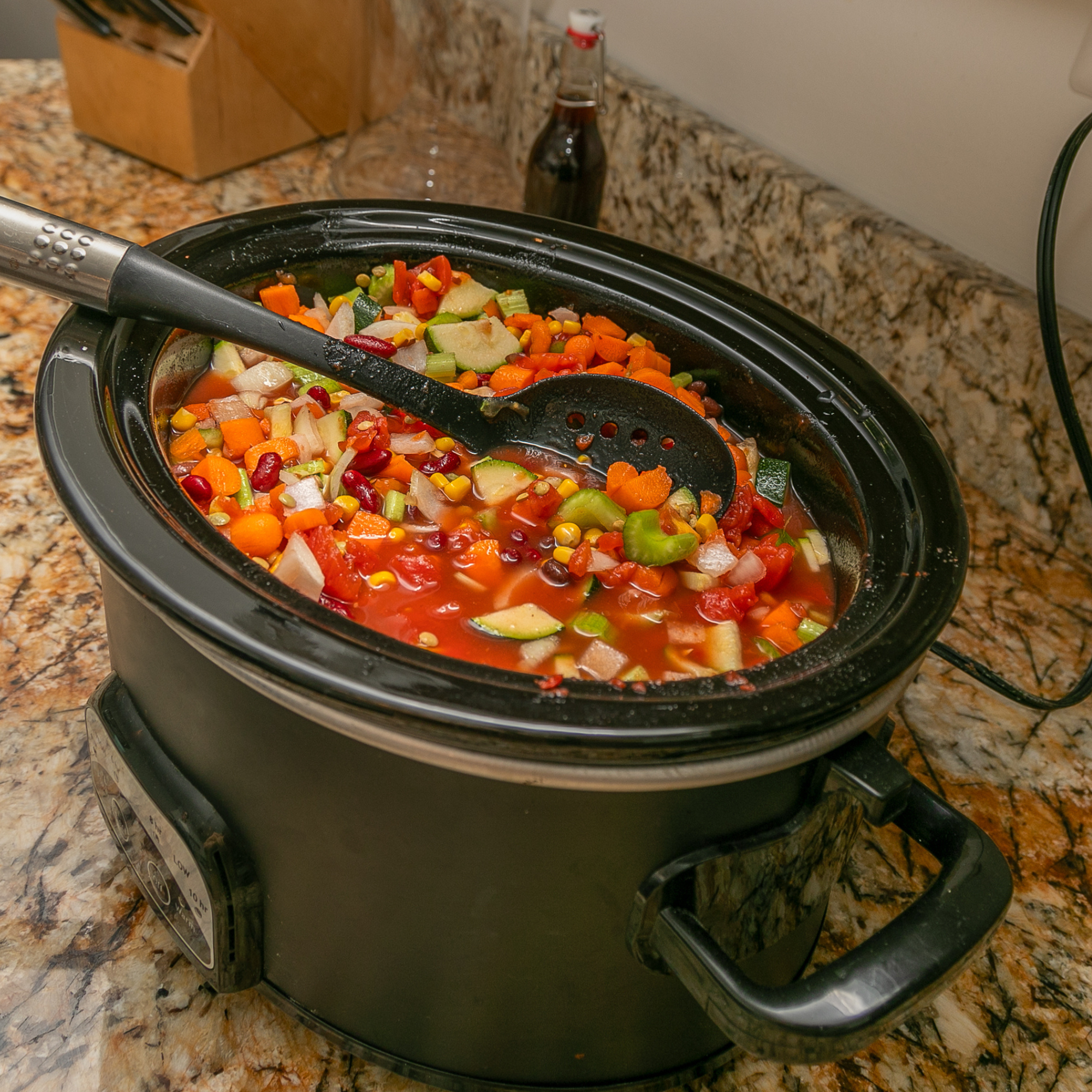 High-angle view of a crock pot with vegetable soup ingredients and a stirring spoon. - stock photo.