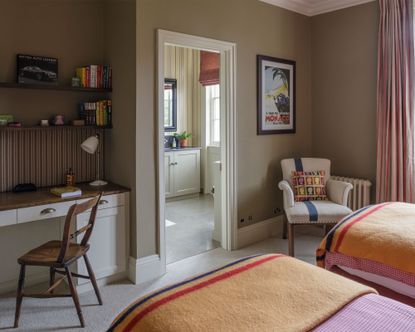 bedroom, twin beds, orange and pink bedding, khaki painted walls, desk built into alcove space, cream armchair in corner beside window