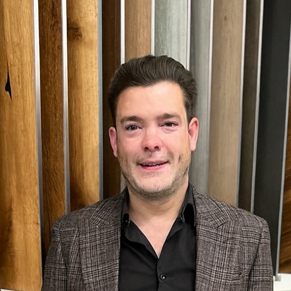 man standing in front of wooden boards wearing brown jacket and black shirt