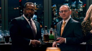 Wendell Pierce and Michael Emerson in Season 2 Episode 8 of Elsbeth standing by a bar with skyscrapers behind them.