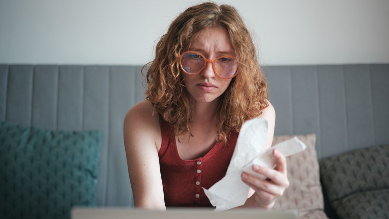 Worried girl holding a stack of student loan bills and looking at her laptop