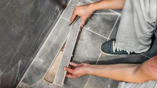 Person placing grey rectangular tile into shower floor
