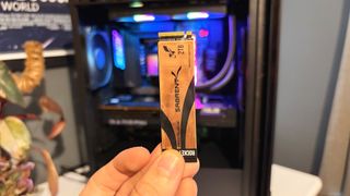 An image of a Sabrent NVMe SSD held up on front of a gaming PC.