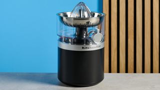 KitchenAid Go Cordless Citrus Juicer in matte black photographed in front of a blue background.