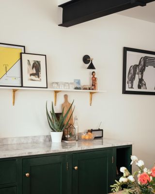 Marble kitchen counter with green cupboards and wall shelves with decorations on.