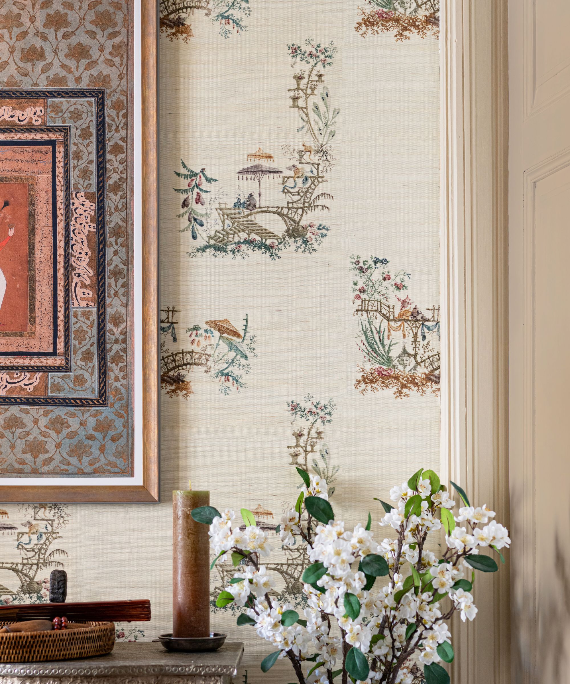 Neutral hallway with cream wallpaper featuring delicate scenic prints of trees, bridges, and pagodas, paired with a vase of white blossom branches.