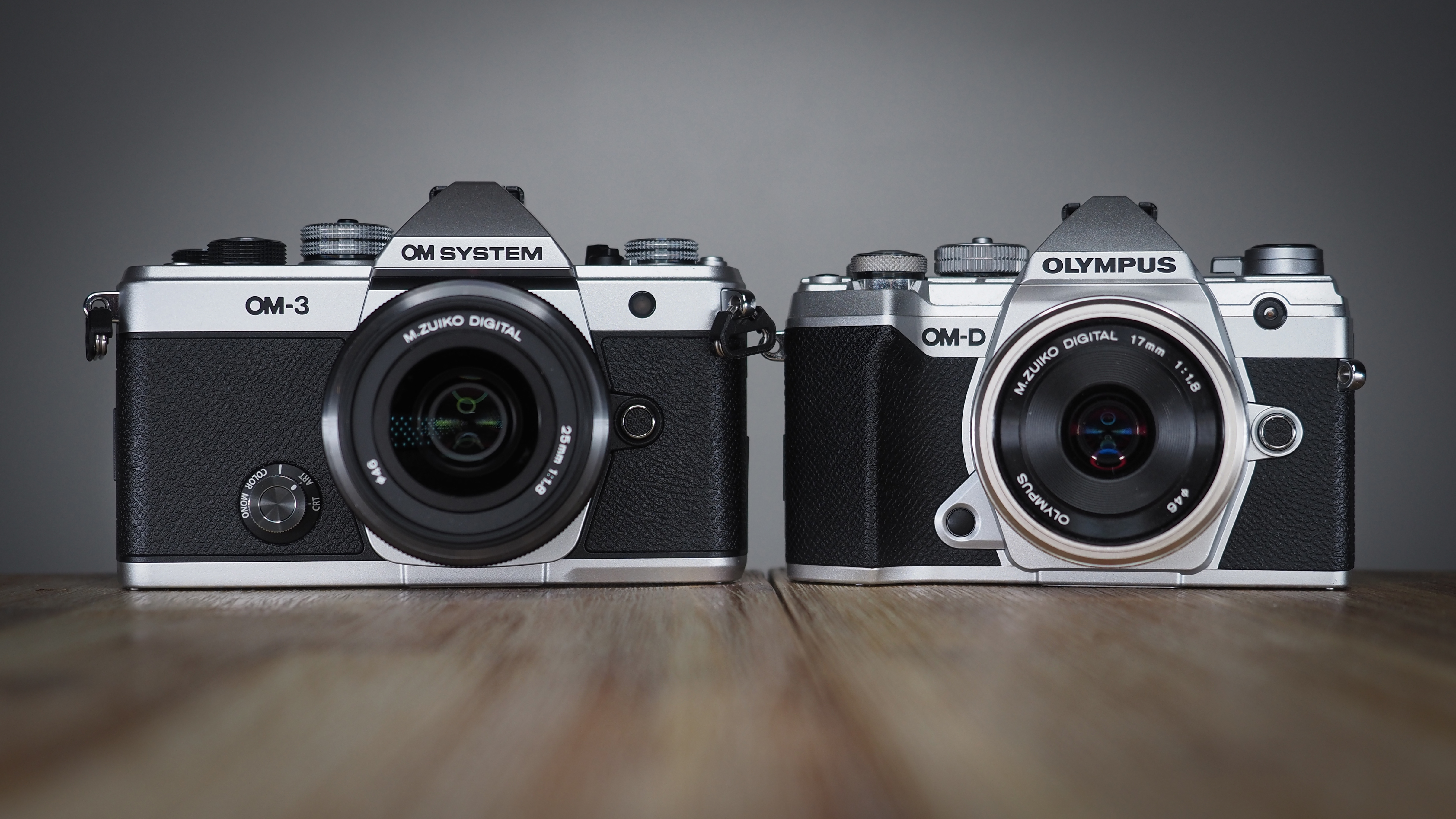 OM System OM-3, next to an Olympus OM-D E-M5 Mark III, on a wooden surface