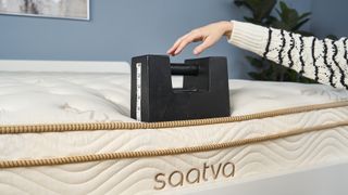 Our reviewer places a black 25kg cast iron weight on the edge of the Saatva Classic mattress to test its edge support