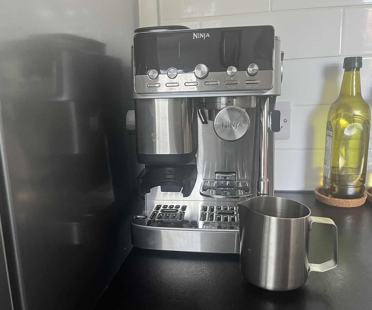 The Ninja luxe cafe mini plus espresso machine on a black kitchen counter with a stainless steel milk jug