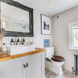 Bathroom with sink, grey cupboards, wall mirror, toilet and patterned floor.