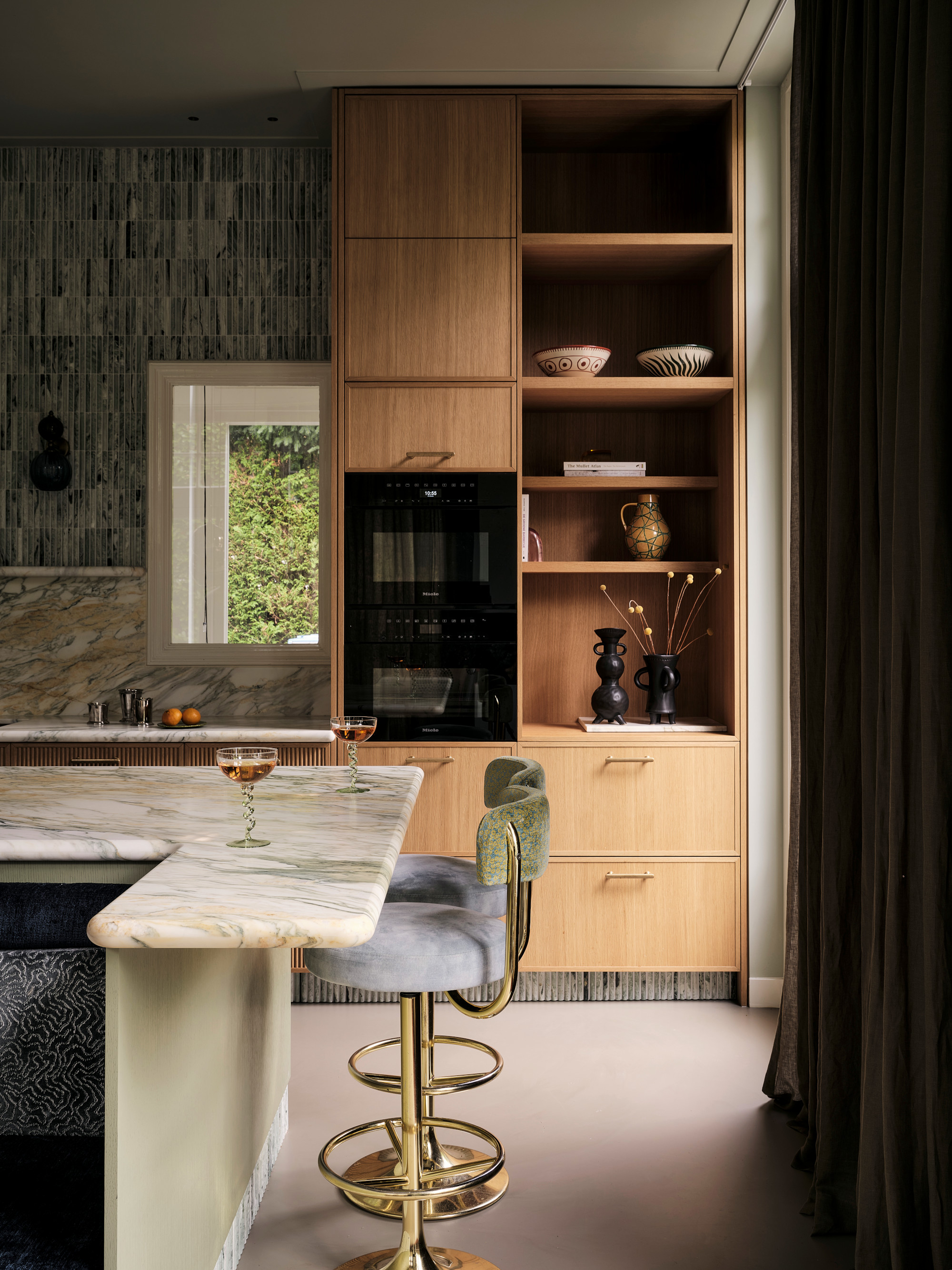 Edge of a kitchen with soft-edged marble countertop, pale blue and gold bar stools, wood kitchen joinery