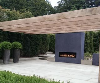 An outdoor fireplace built into a wall with a wooden pergola over the top