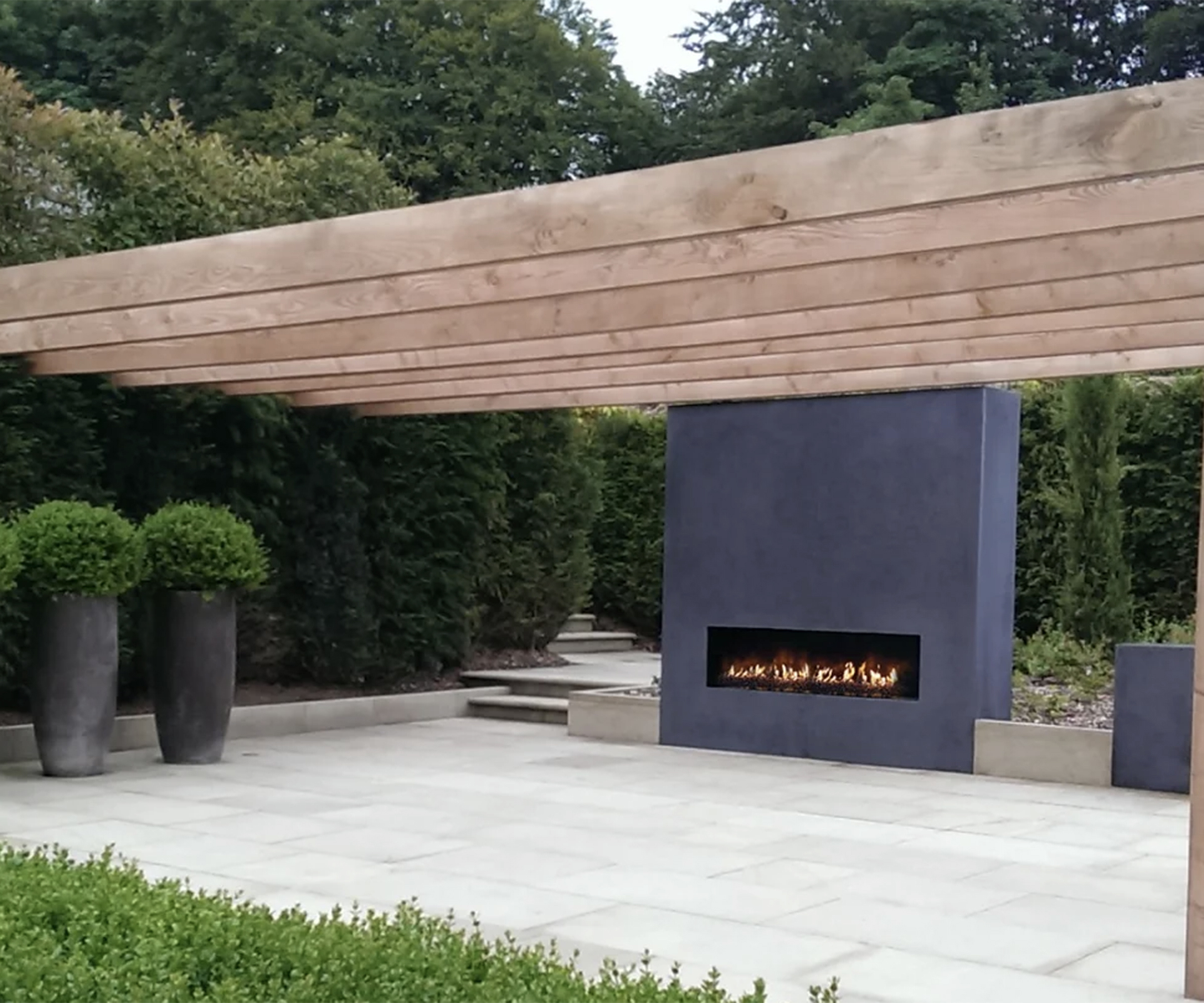 An outdoor fireplace built into a wall with a wooden pergola over the top