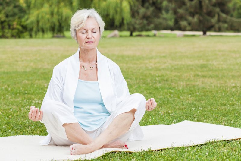 An older woman sits in a green field, meditating.