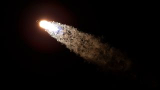 looking up at the fiery plume created by a rocket launching into a dark night sky