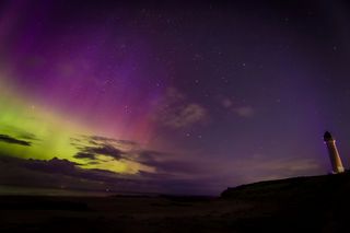 green and purple aurora in the sky with a small lighthouse on the right of the image.