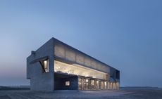 Dusky image of the Seashore Library lit up, sand surrounds the building, clear dusk sky