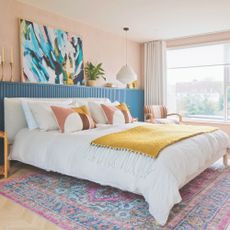 Colourful master bedroom with large bed, wall panelling, colourful artwork and multicoloured rug beneath the bed