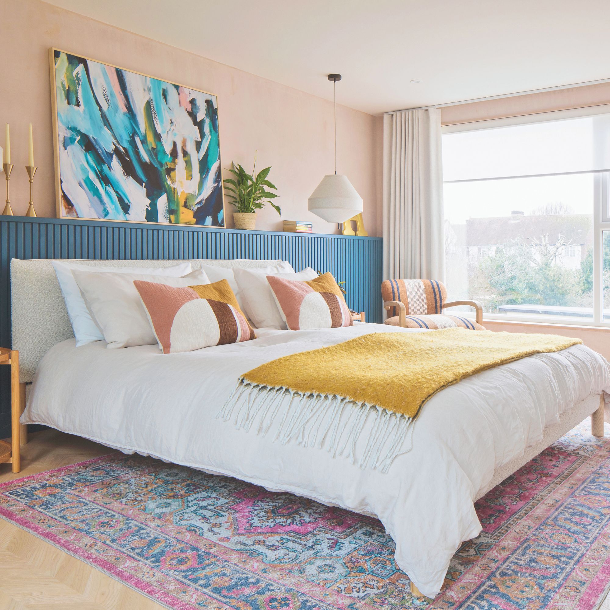 Colourful master bedroom with large bed, wall panelling, colourful artwork and multicoloured rug beneath the bed