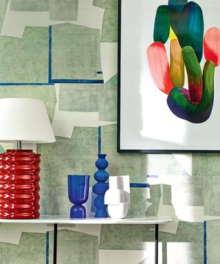 Colorful entryway with green abstract wallpaper, framed artwork, white shelf, red table lamp, decorative ornaments