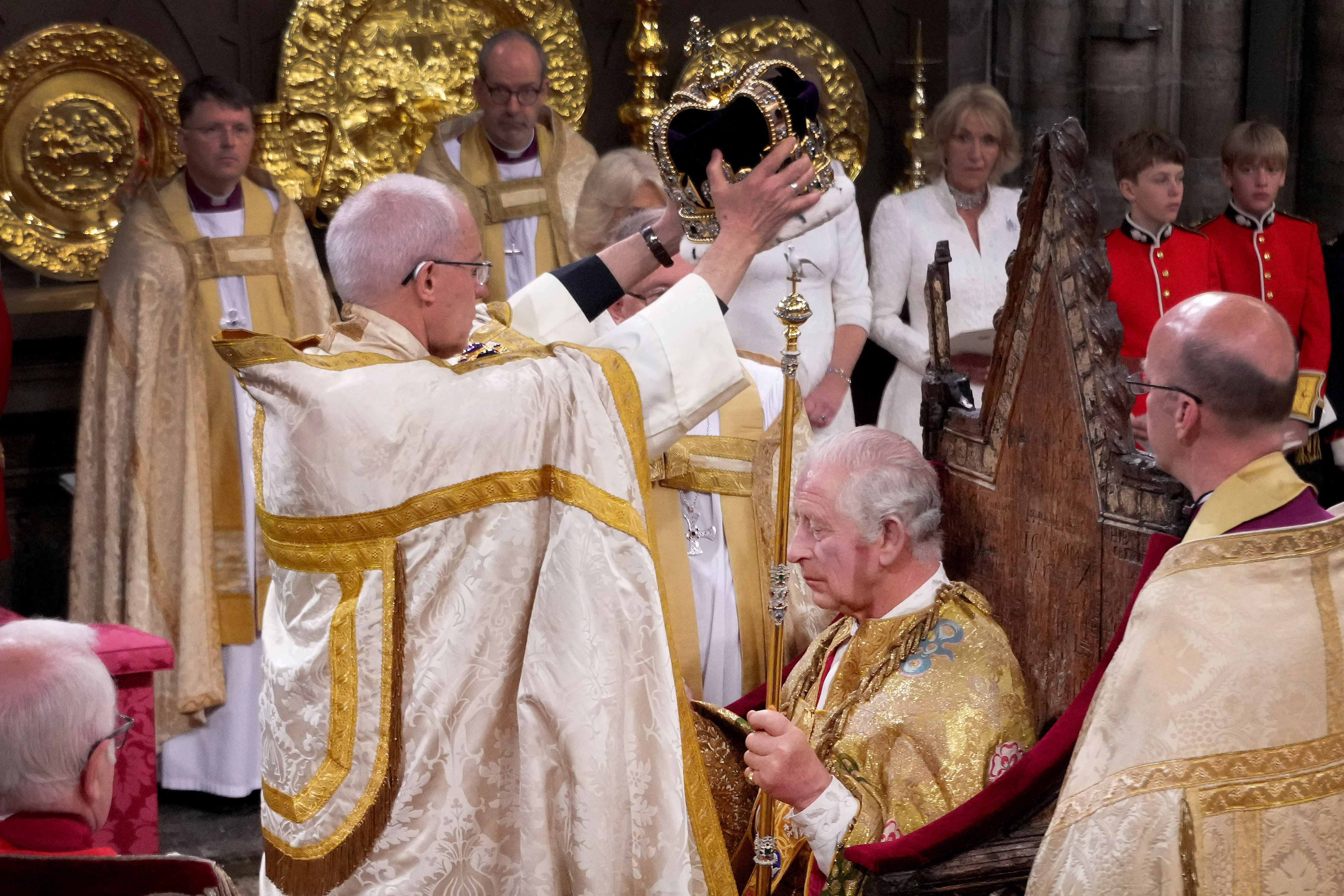 King Charles sitting in a throne being crowned at Westminster Abbey