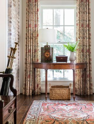 entryway with exposed brick wall and oriental rug and half moon console table in dark wood with lamp and patterned curtains umbrella stand and traditional wood chair