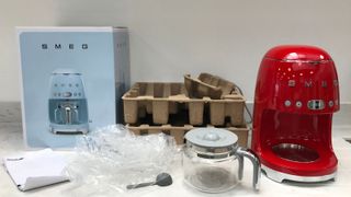 The red Smeg drip coffee maker with all of the plastic and cardboard packaging around it