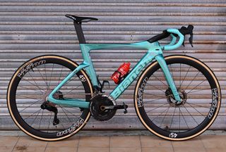 A blue Bianchi road bike is up against a garage door background side on