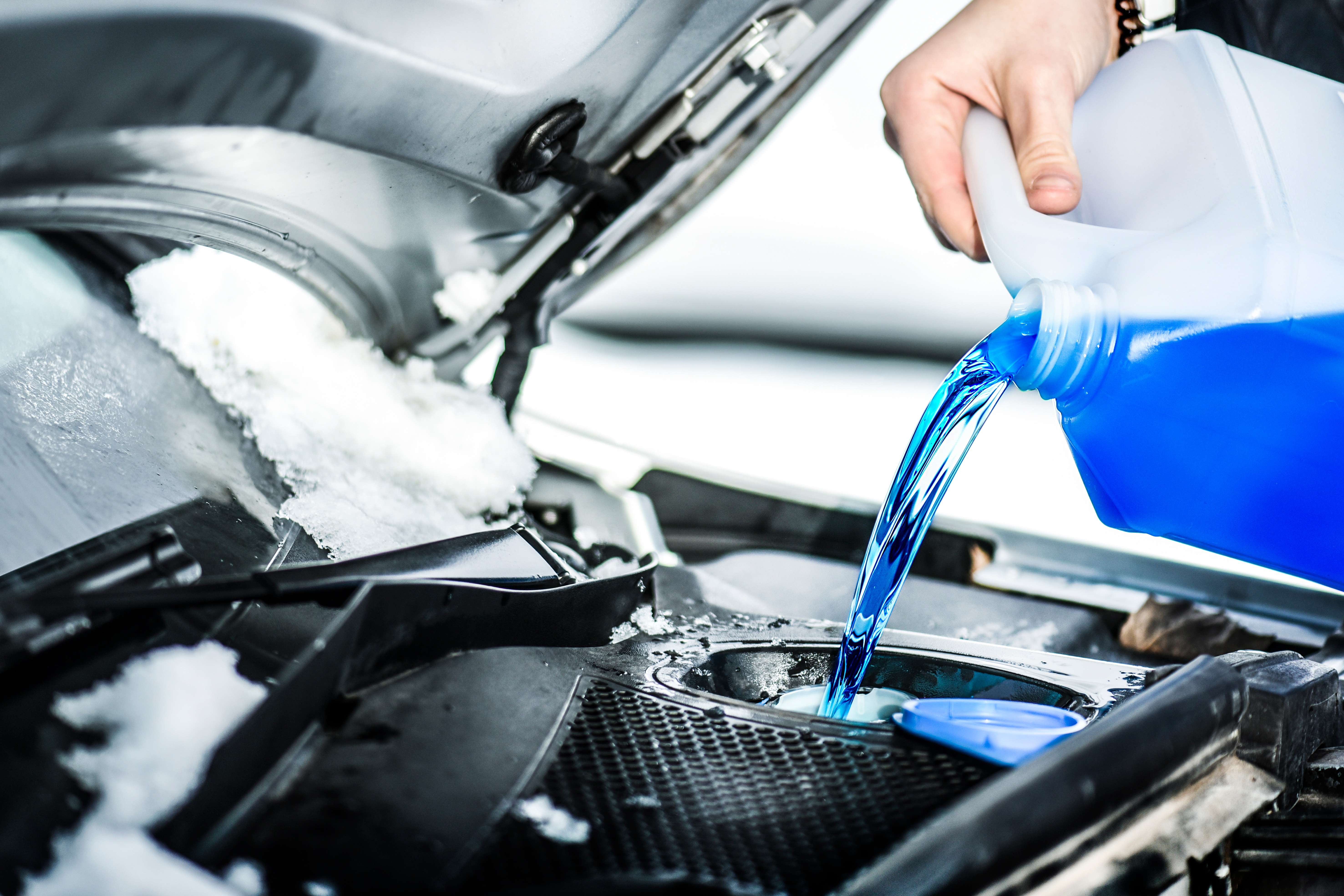 pouring windshield wiper fluid into snow-covered car