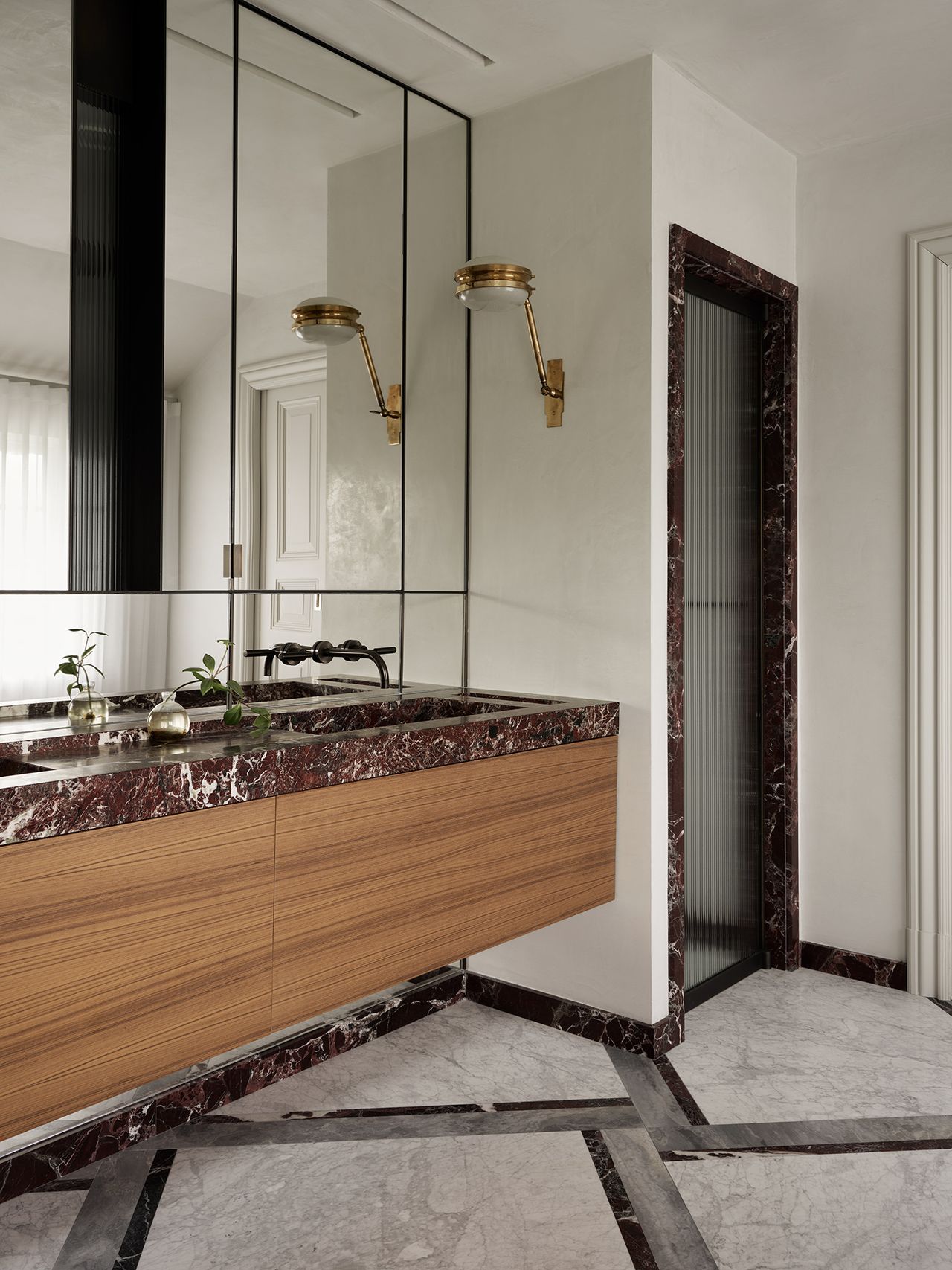 marble bathroom with mixed pattern on floor, red marble trim and counter, timber vanity, enclosed shower, and gold wall sconce