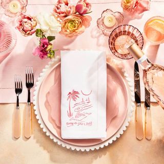 Pink tablescape set up with plates, cutlery and an embroidered napkin.