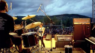 Band playing live on stage with view behind the drummer