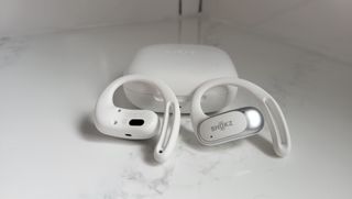 White Shokz OpenFit Air earbuds propped up on white case on marble countertop