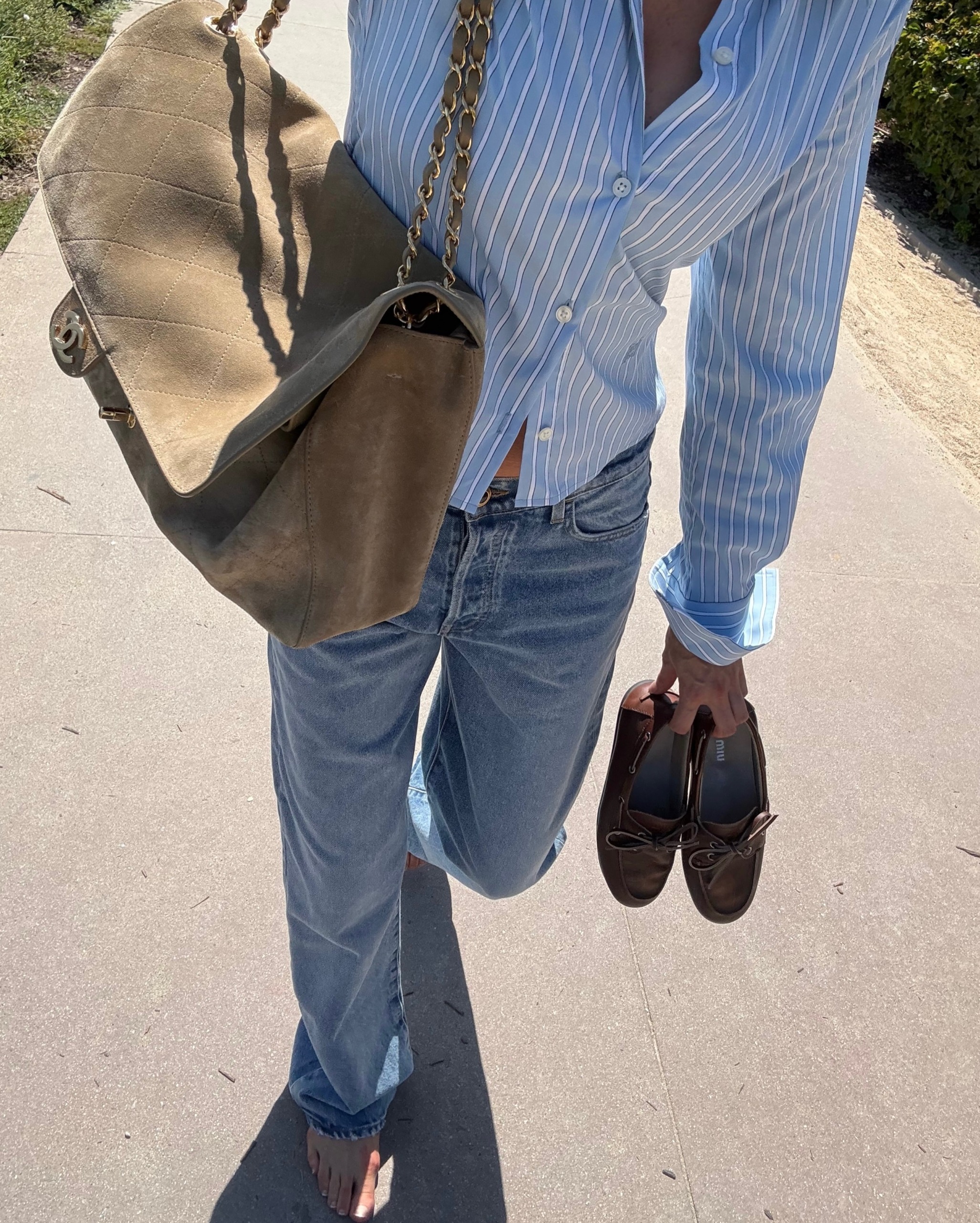 Elsa Hosk carrying a beige suede Chanel Maxi Flap bag with a blue button-down shirt and jeans.