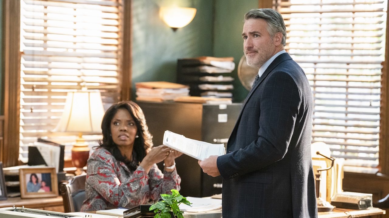 Mary Jo seated at her desk and Dalton standing in front of it with a file in hand on NCIS: Origins