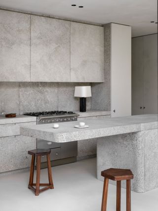 Grey stone kitchen with cantilevered island and dark wood bar stools