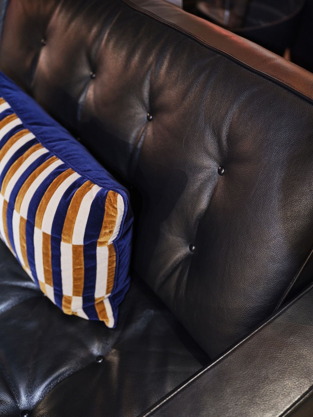 Close-up of the Heal&rsquo;s Hepburn sofa&rsquo;s black leather backrest, showing its buttoned upholstery, natural creasing and tailored finish.
