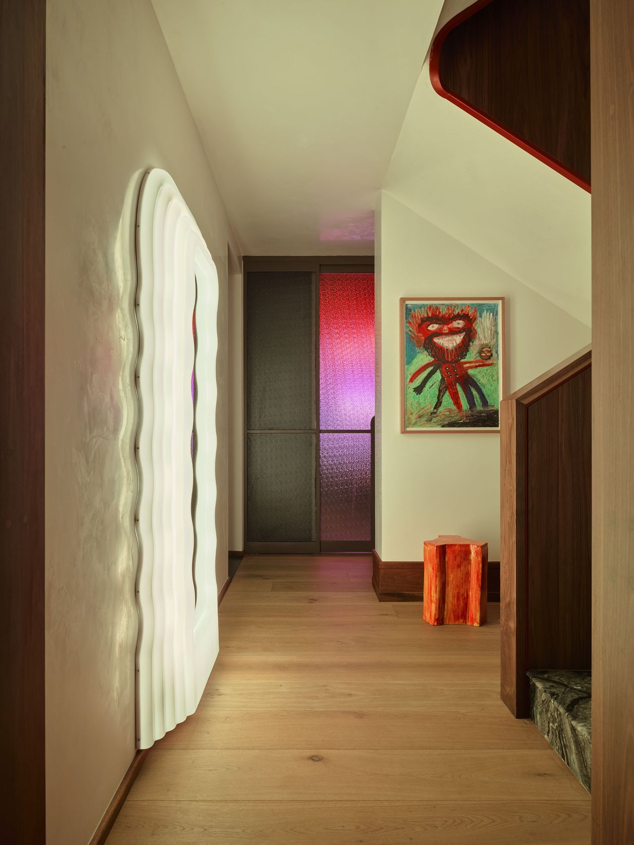 hallway with illuminated mirror, staircase, artwork and colored glass wall